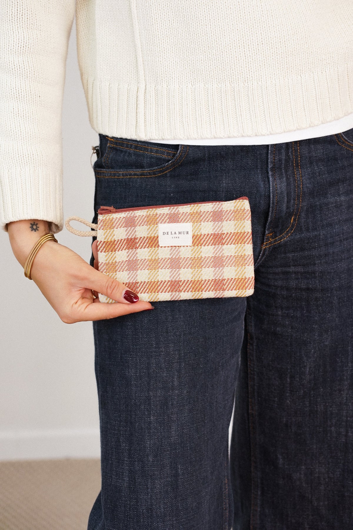 Model holding DE LA MUR terracotta gingham coin purse at the hip, lifestyle shot