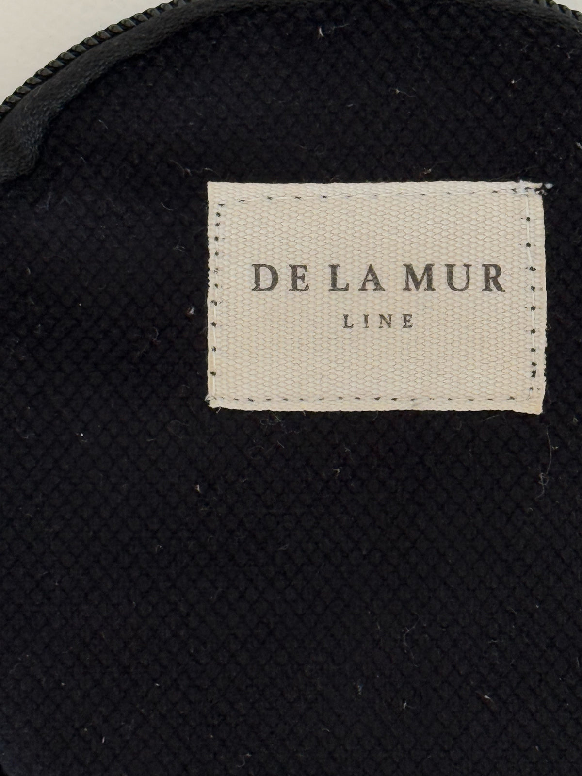 Close-up of black woven fabric and DE LA MUR Line label on Aza coin purse