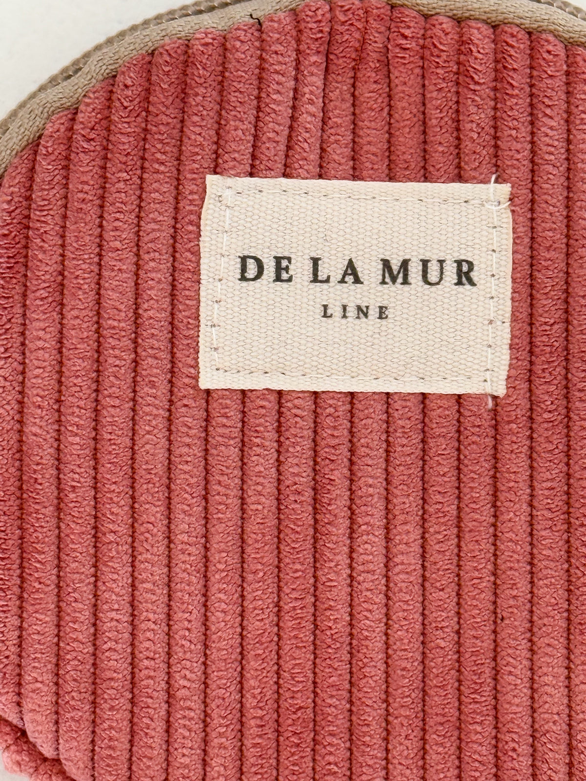 Close-up of dusty rose corduroy and DE LA MUR Line label on coin purse