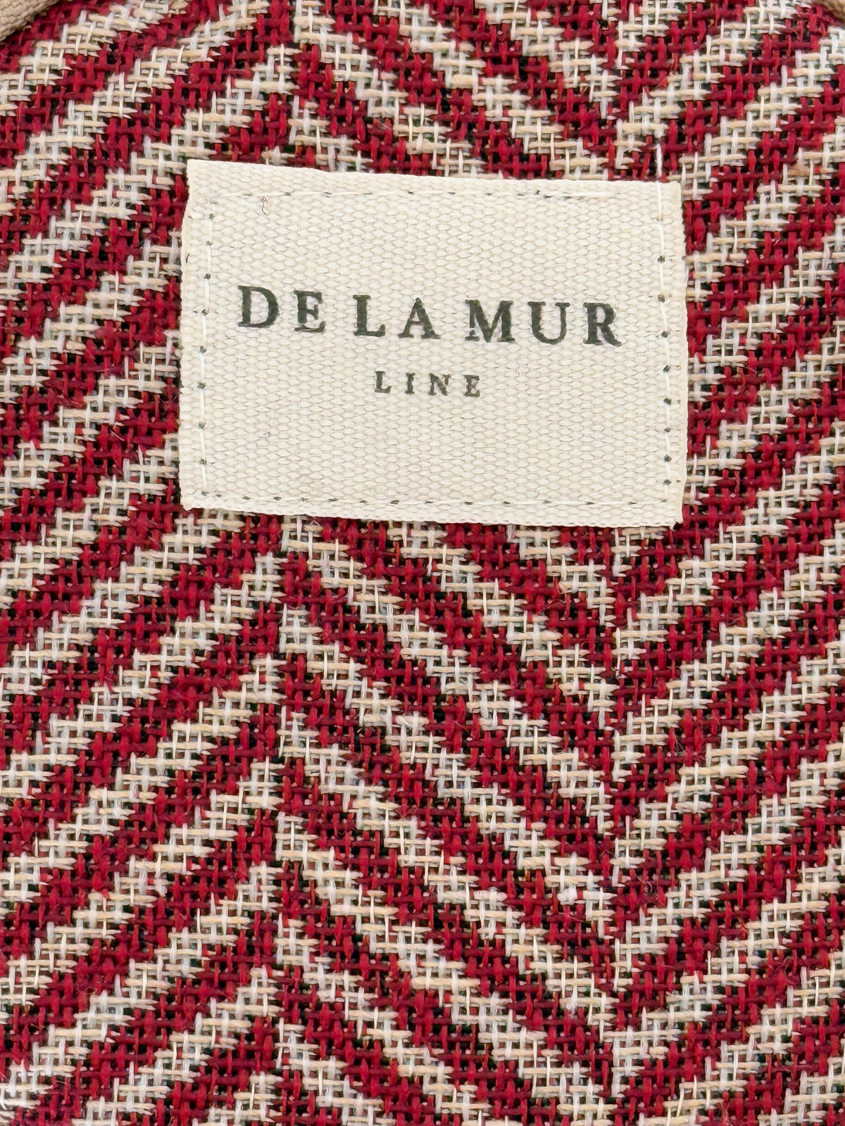 Close-up of the burgundy herringbone weave and DE LA MUR Line label on the coin purse