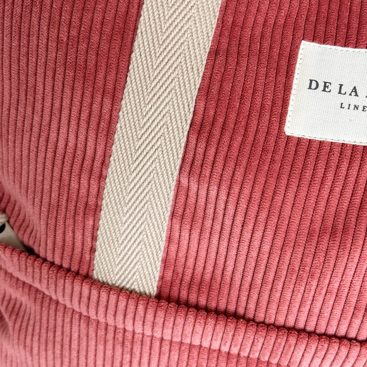 Close-up of the coral corduroy texture and beige herringbone strap on the DE LA MUR backpack