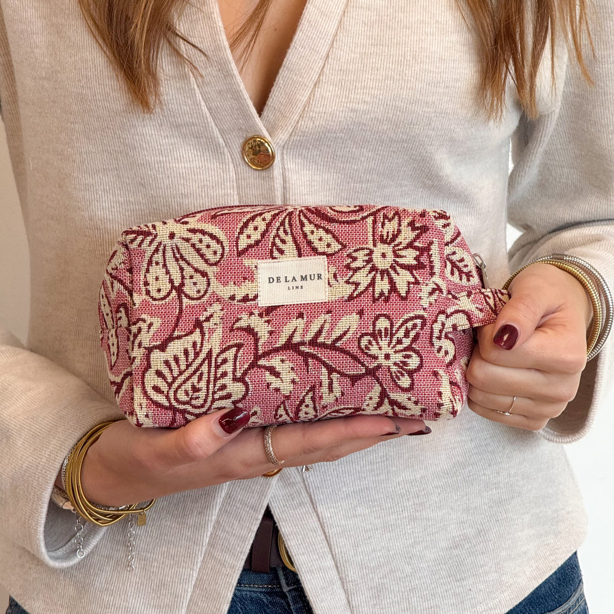 Model holding the ecru and pink floral DE LA MUR squared makeup bag
