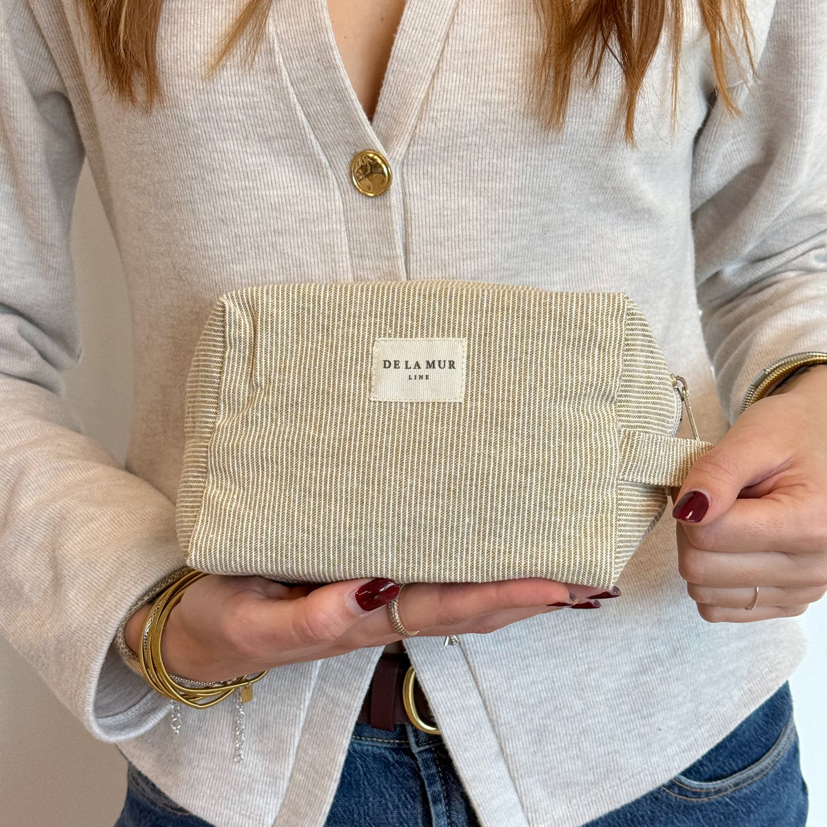 Model holding the mustard textured striped DE LA MUR squared makeup bag