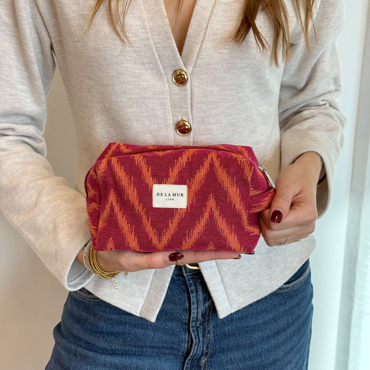 Model holding the DE LA MUR Fuego zigzag jacquard makeup bag