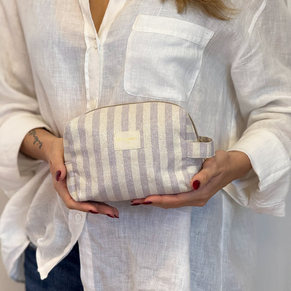 Model holding the DE LA MUR Lulil lilac and gold striped makeup bag