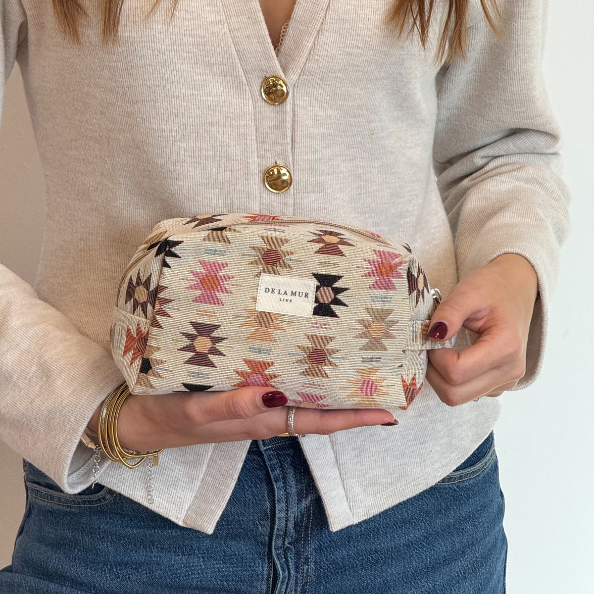 Model holding the DE LA MUR Royal Aztec jacquard makeup bag, lifestyle shot