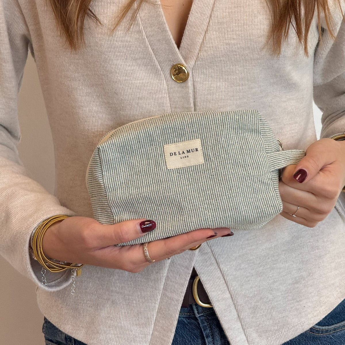 Model holding the DE LA MUR Teo green striped makeup bag, lifestyle shot