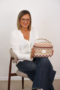 Seated woman holding the DE LA MUR multicolor zigzag jacquard makeup bag, lifestyle view