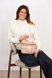 Woman seated holding the DE LA MUR Zia gingham jacquard makeup bag, lifestyle shot