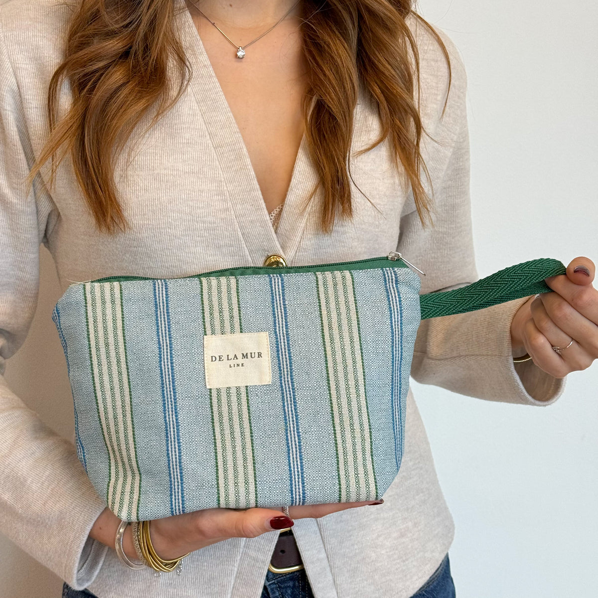 Model holding the green and blue striped DE LA MUR Cata makeup bag