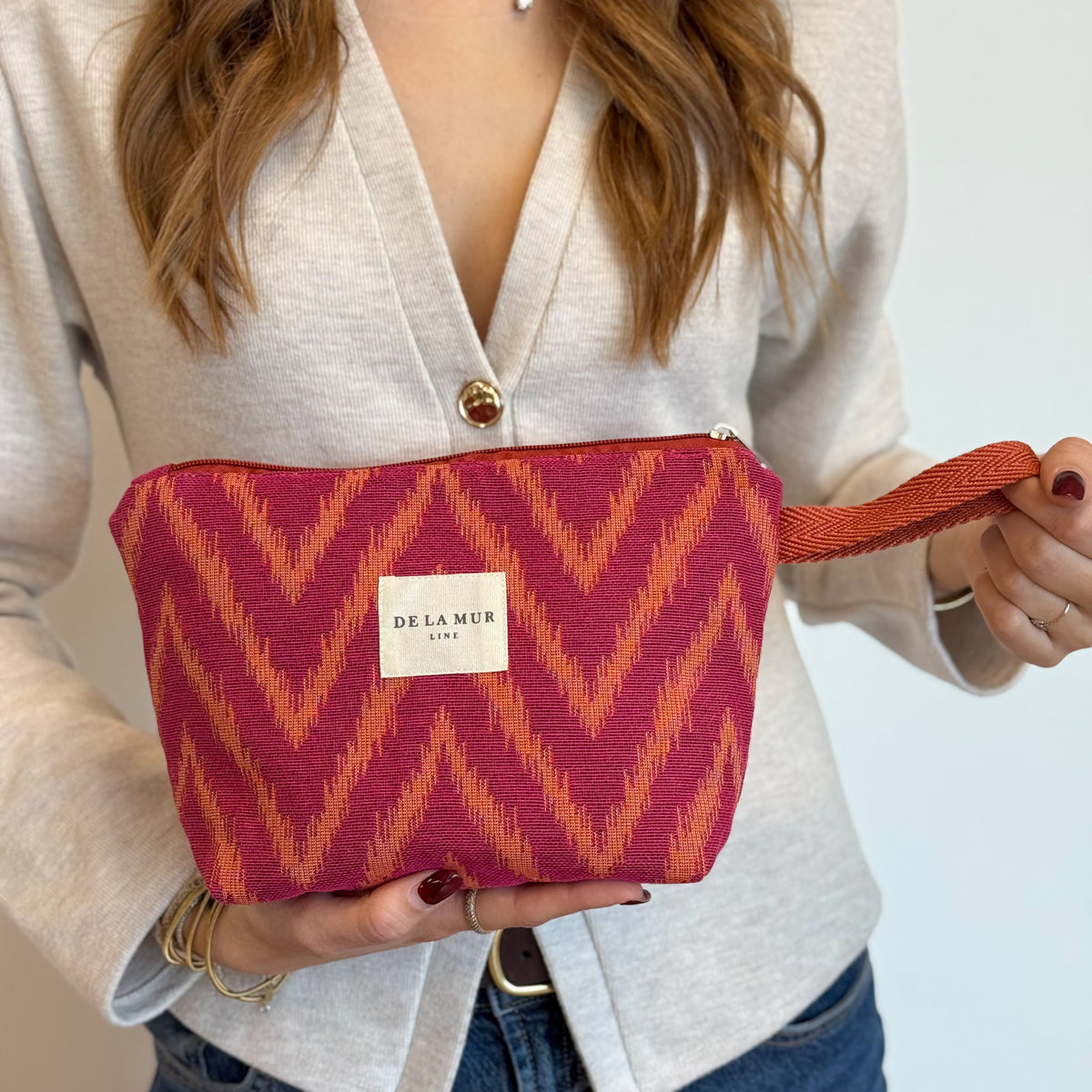 Model holding the pink and orange zigzag DE LA MUR Fuego makeup bag
