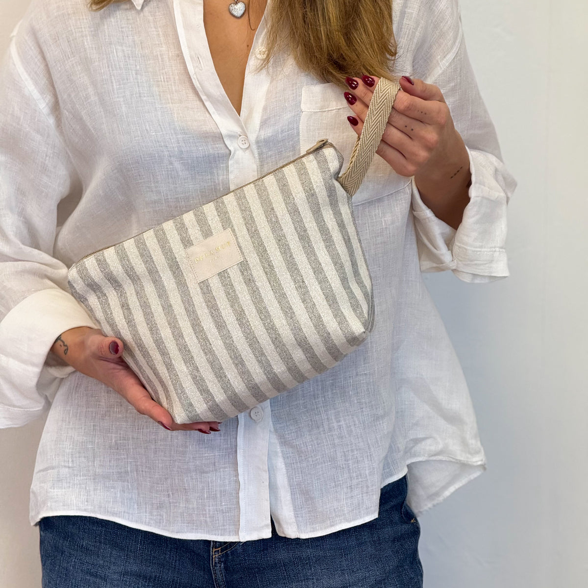 Model holding the beige and grey striped DE LA MUR Lugris makeup bag