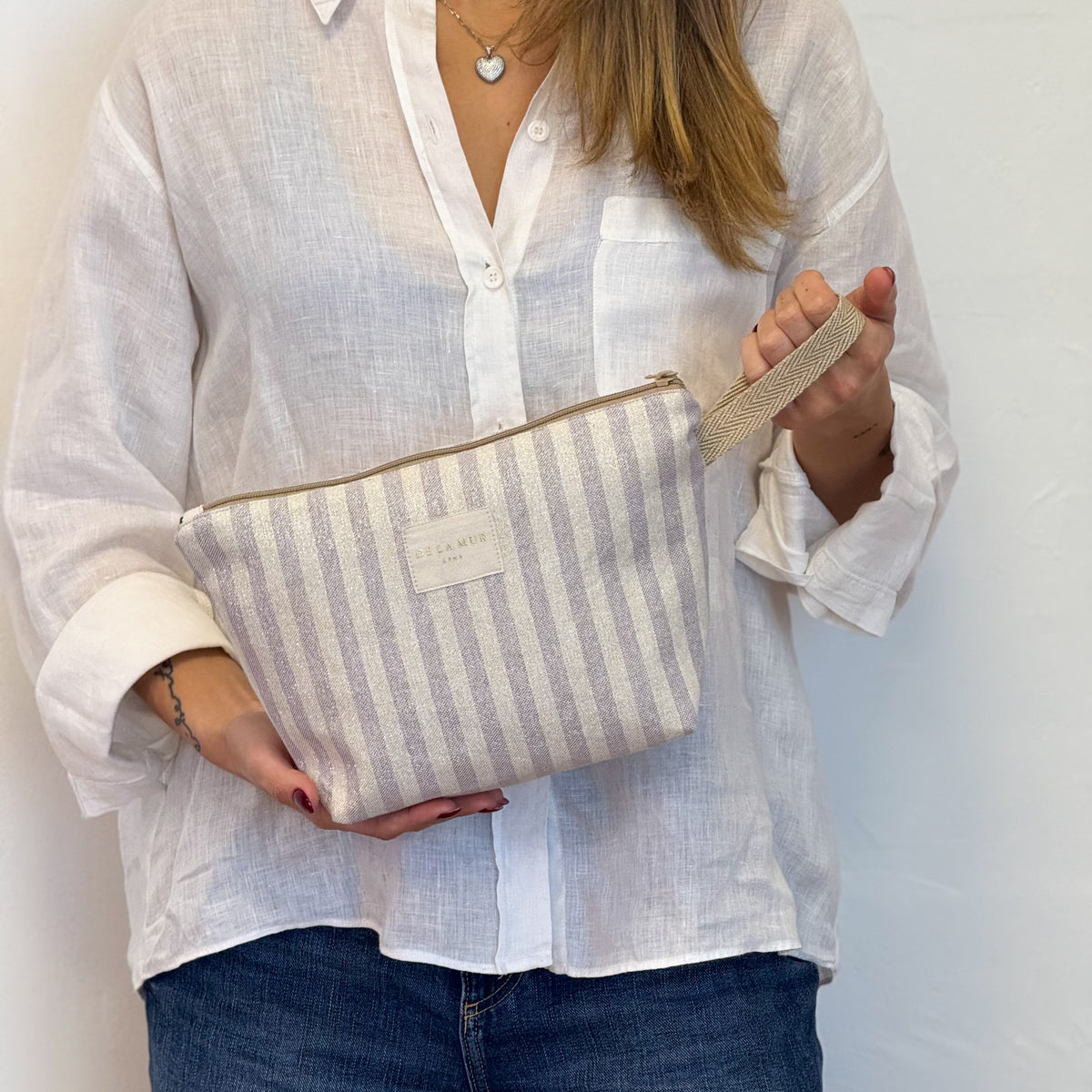 Model holding the beige and ecru striped DE LA MUR Lulil makeup bag