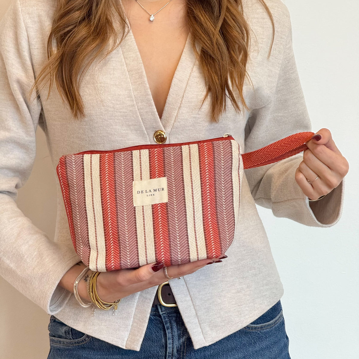 Model holding the burgundy striped DE LA MUR Make makeup bag by its strap