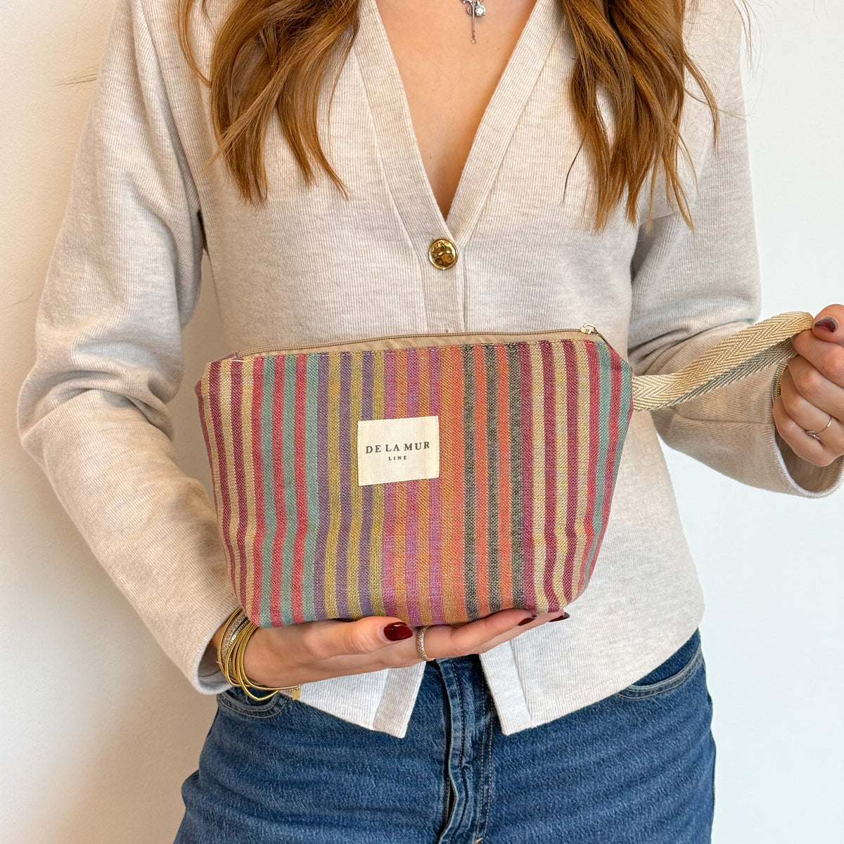 Model holding the multicolor striped DE LA MUR Maria makeup bag by its strap