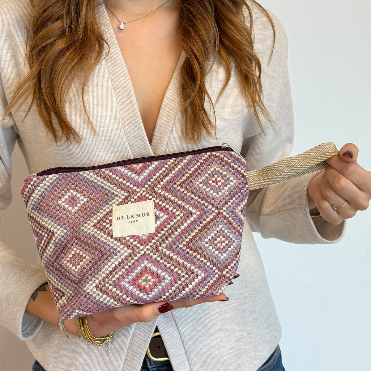 Model holding the diamond-pattern DE LA MUR Nana makeup bag by its strap