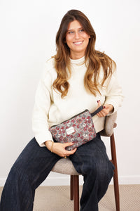 Woman holding the burgundy and gray floral DE LA MUR makeup bag by its strap