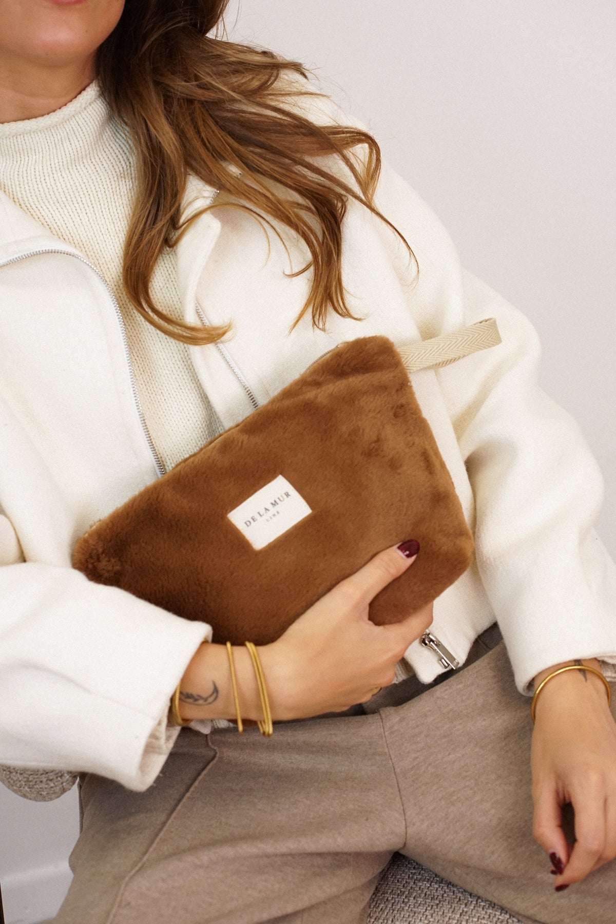 Model cradling the DE LA MUR camel faux fur makeup bag, lifestyle close-up