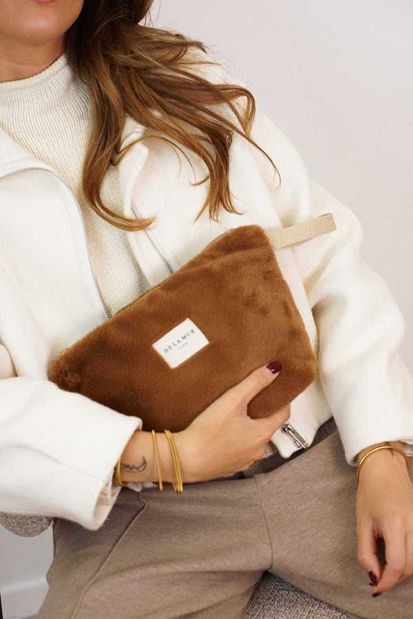 Model cradling the DE LA MUR camel faux fur makeup bag, lifestyle close-up