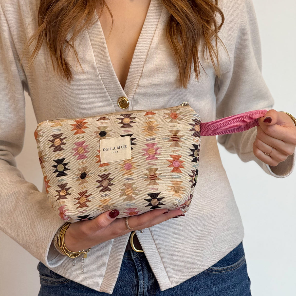 Model holding the DE LA MUR geometric jacquard makeup bag by its pink strap