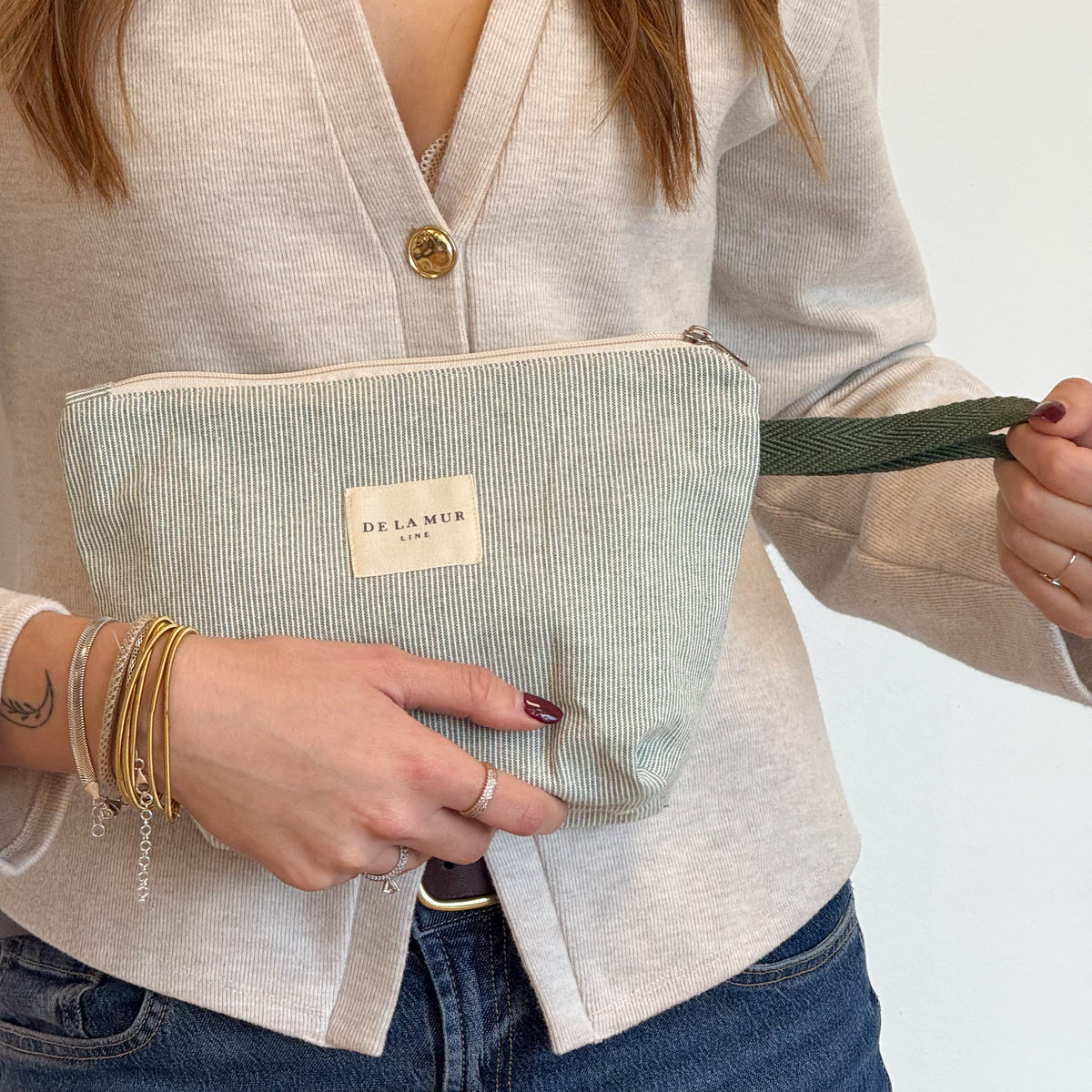 Model holding the DE LA MUR green striped makeup bag by its side strap