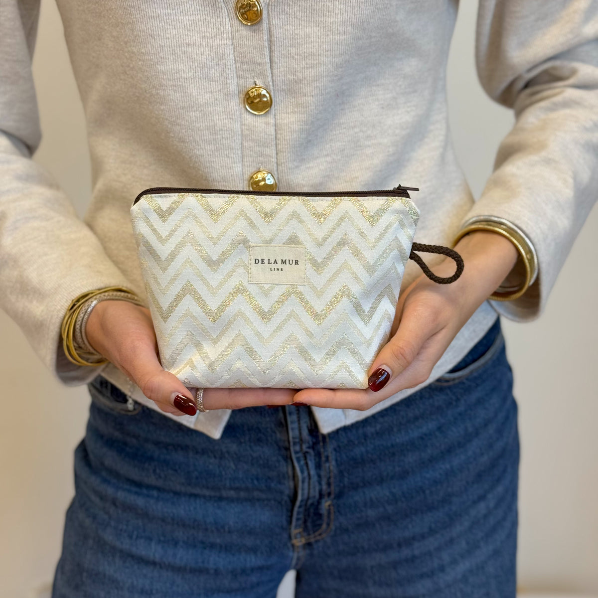 Model holding the DE LA MUR gold zigzag small makeup bag in both hands