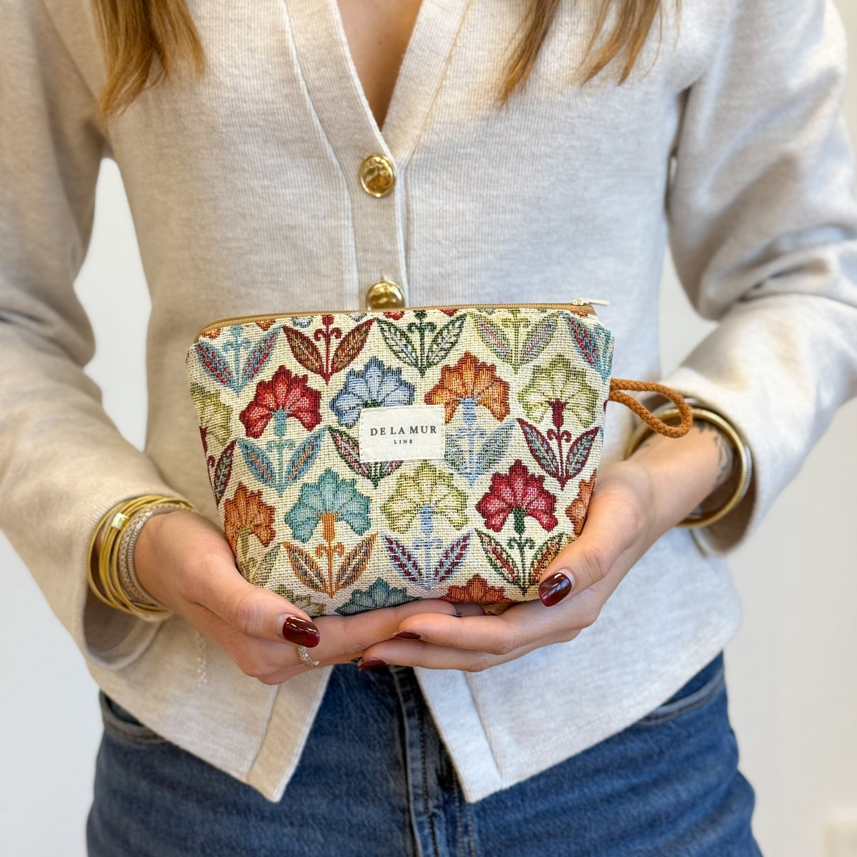 Model holding the DE LA MUR multicolor floral jacquard makeup bag in both hands
