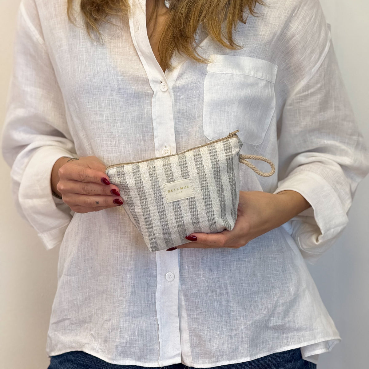 Model holding the DE LA MUR beige striped makeup bag against a white shirt