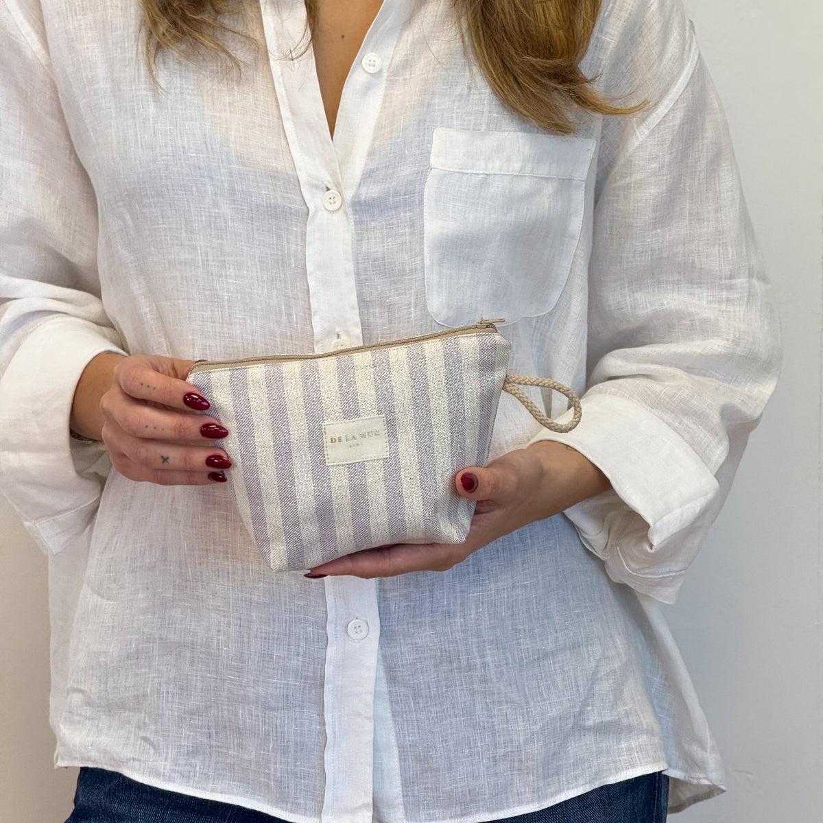 Model holding the DE LA MUR beige and lilac striped makeup bag
