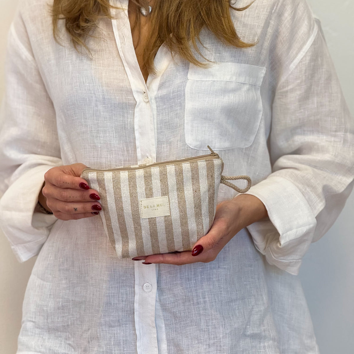 Model holding the DE LA MUR beige and mustard striped makeup bag