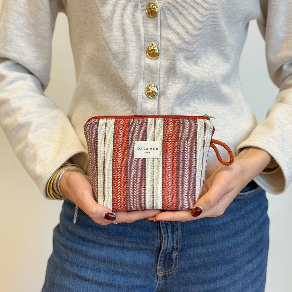 Model holding the DE LA MUR burgundy and red striped jacquard makeup bag