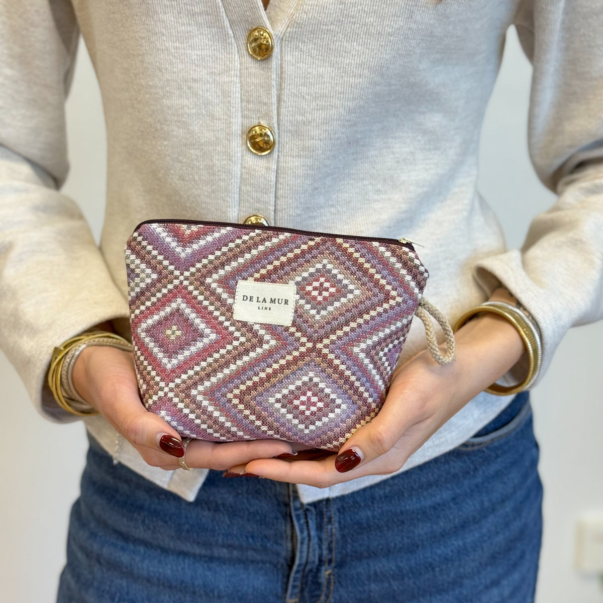 Model holding the DE LA MUR beige and pink geometric diamond jacquard makeup bag