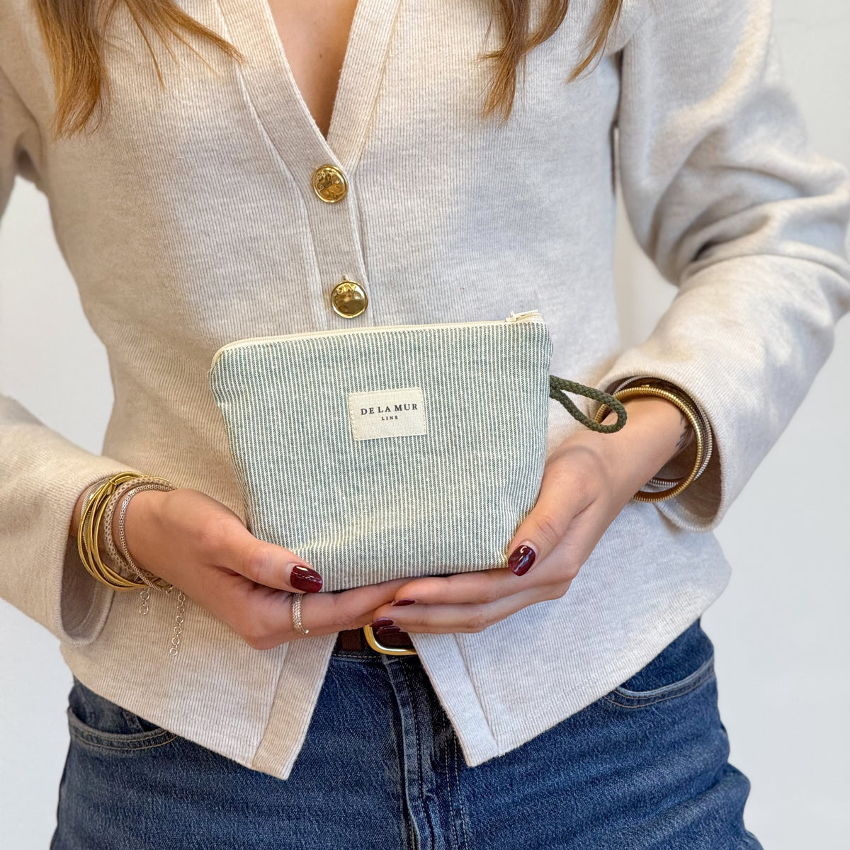 Model holding the DE LA MUR Teo striped makeup bag in both hands