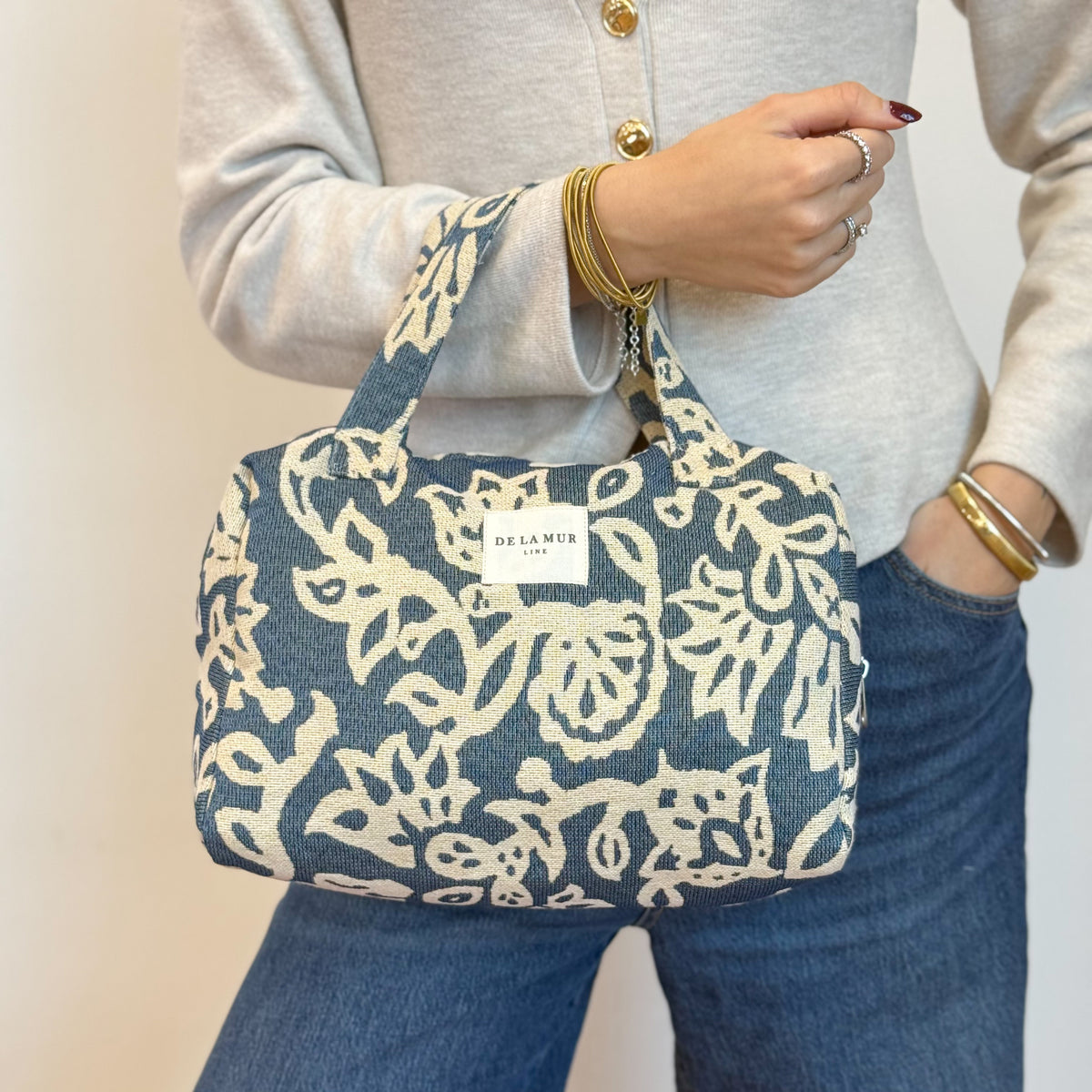 Model carrying the DE LA MUR Akay floral jacquard bag by its top handle