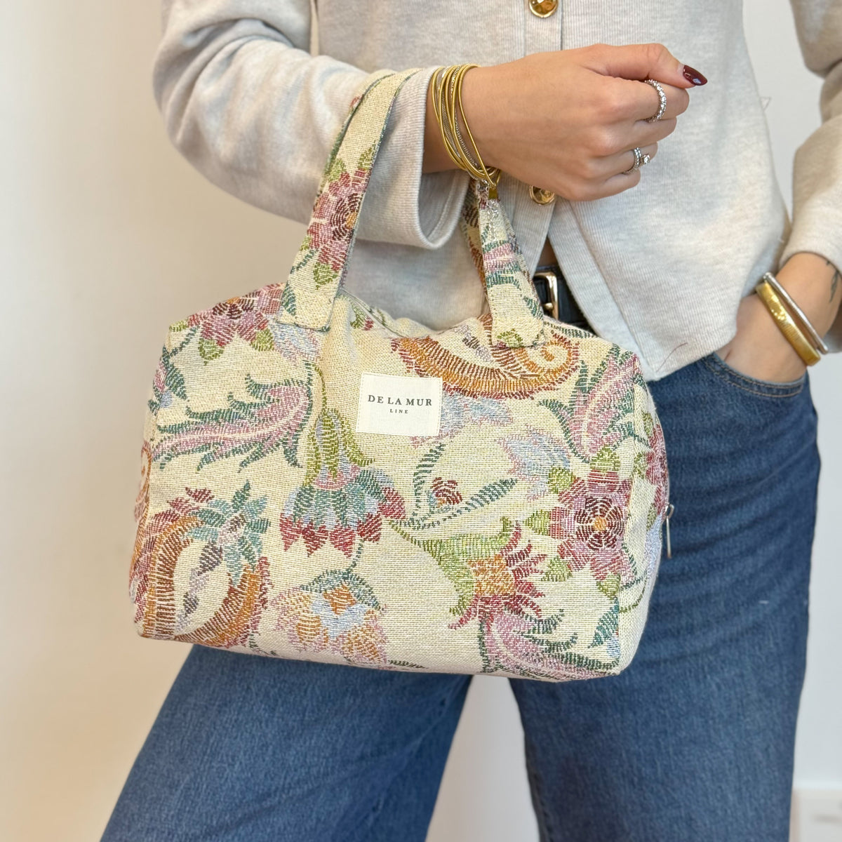 Model carrying the DE LA MUR floral jacquard makeup bag by the handles
