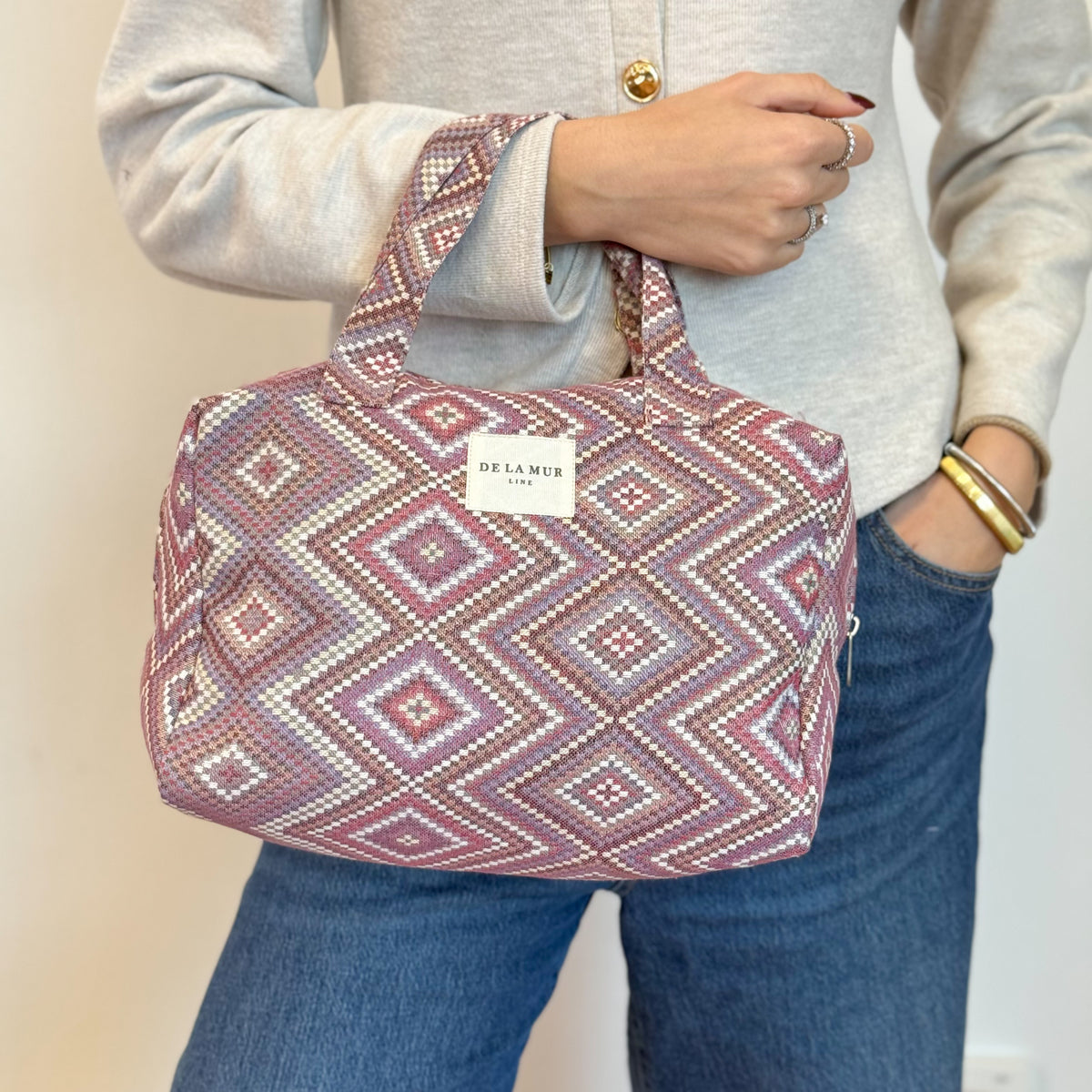 Model carrying the DE LA MUR pink lilac geometric jacquard makeup bag