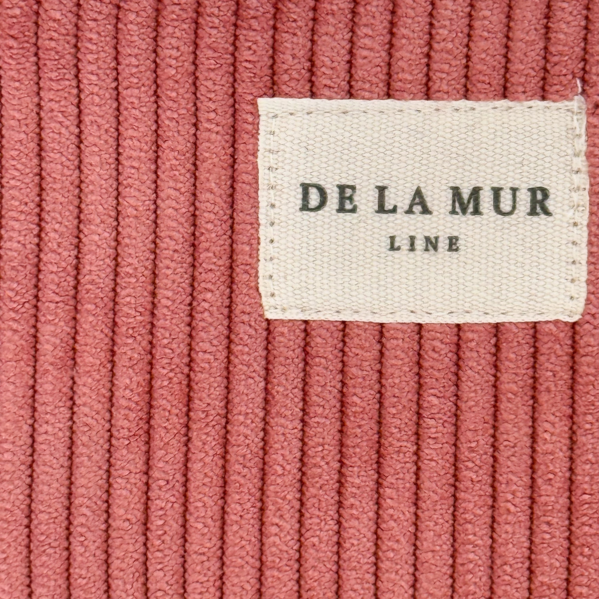 Close-up of coral pink corduroy ribbing and DE LA MUR Line woven label