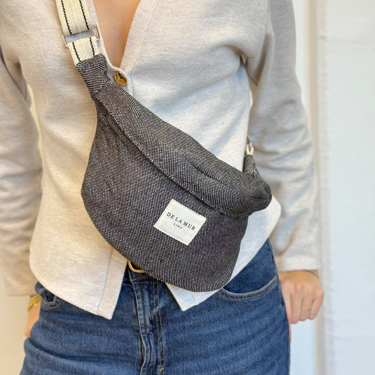 Model wearing the DE LA MUR Sinay off-white herringbone fanny pack at the waist