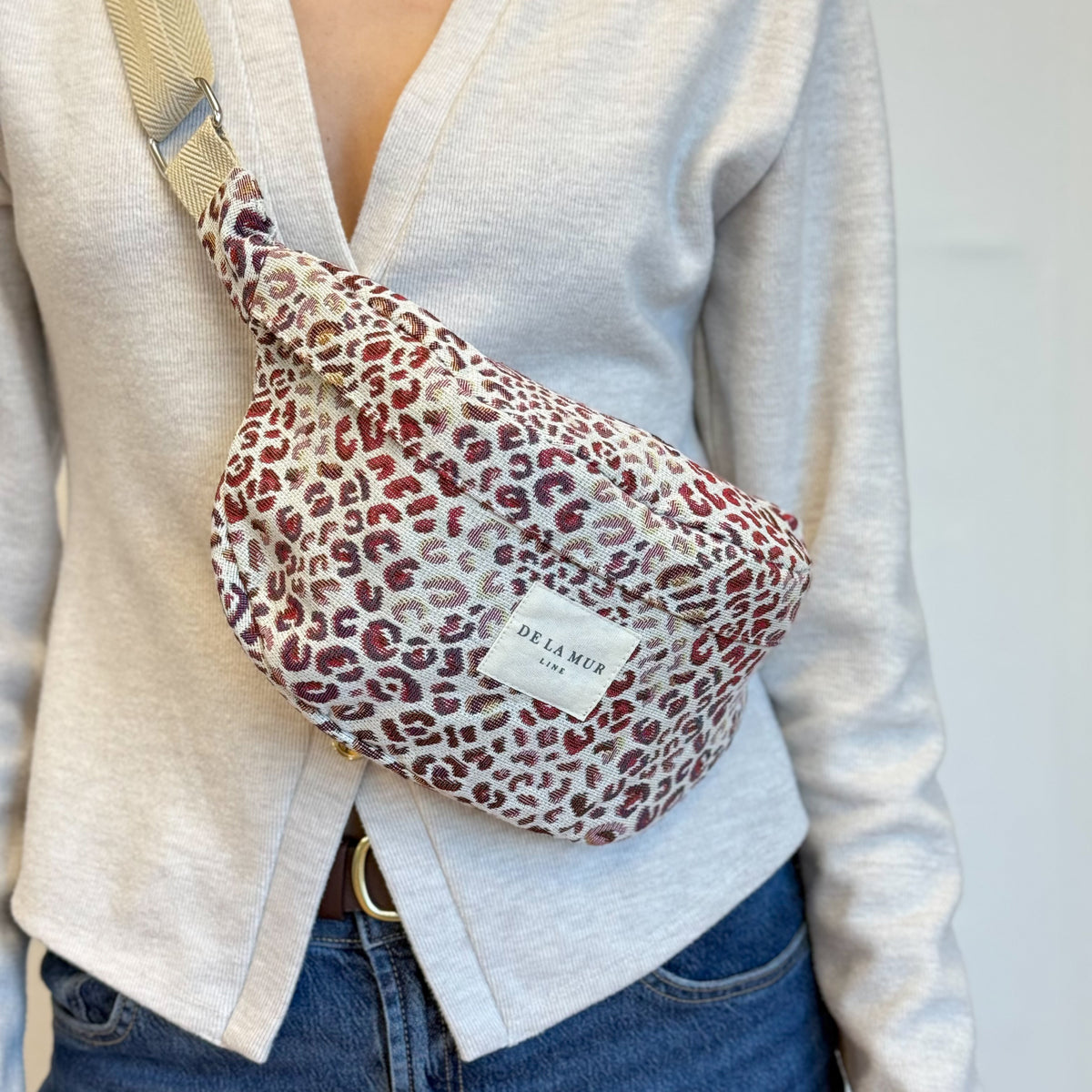 Close-up of DE LA MUR leopard fanny pack worn crossbody over a beige cardigan