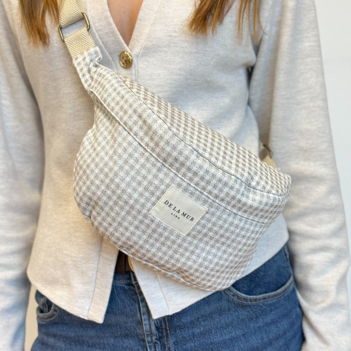 Close-up of DE LA MUR check Vison fanny pack worn crossbody over a cardigan