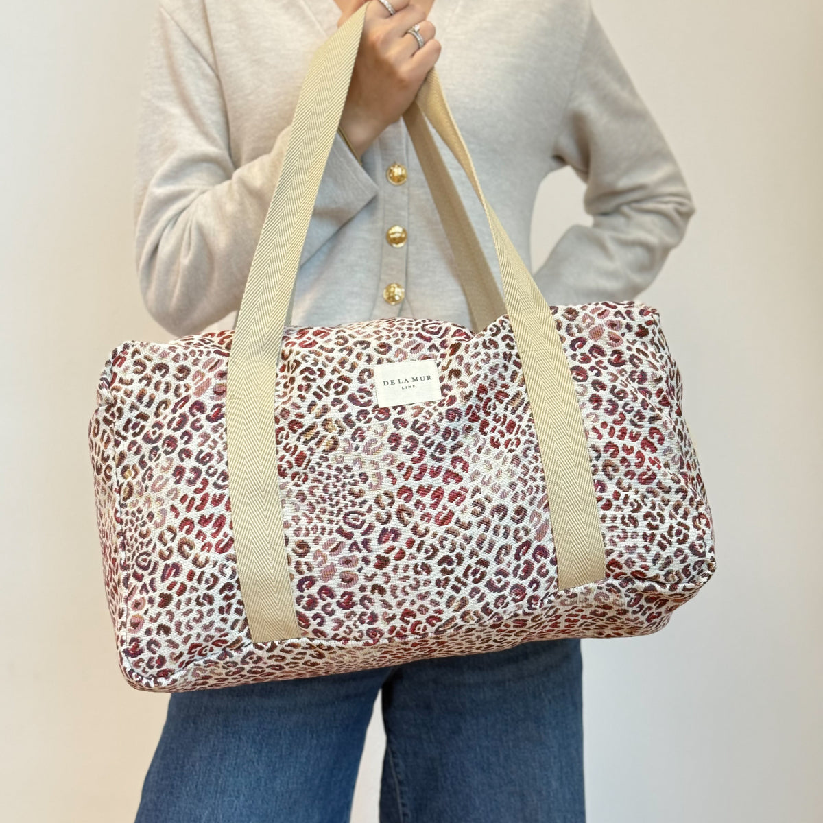 Model holding DE LA MUR leopard print jacquard sports bag by the handles