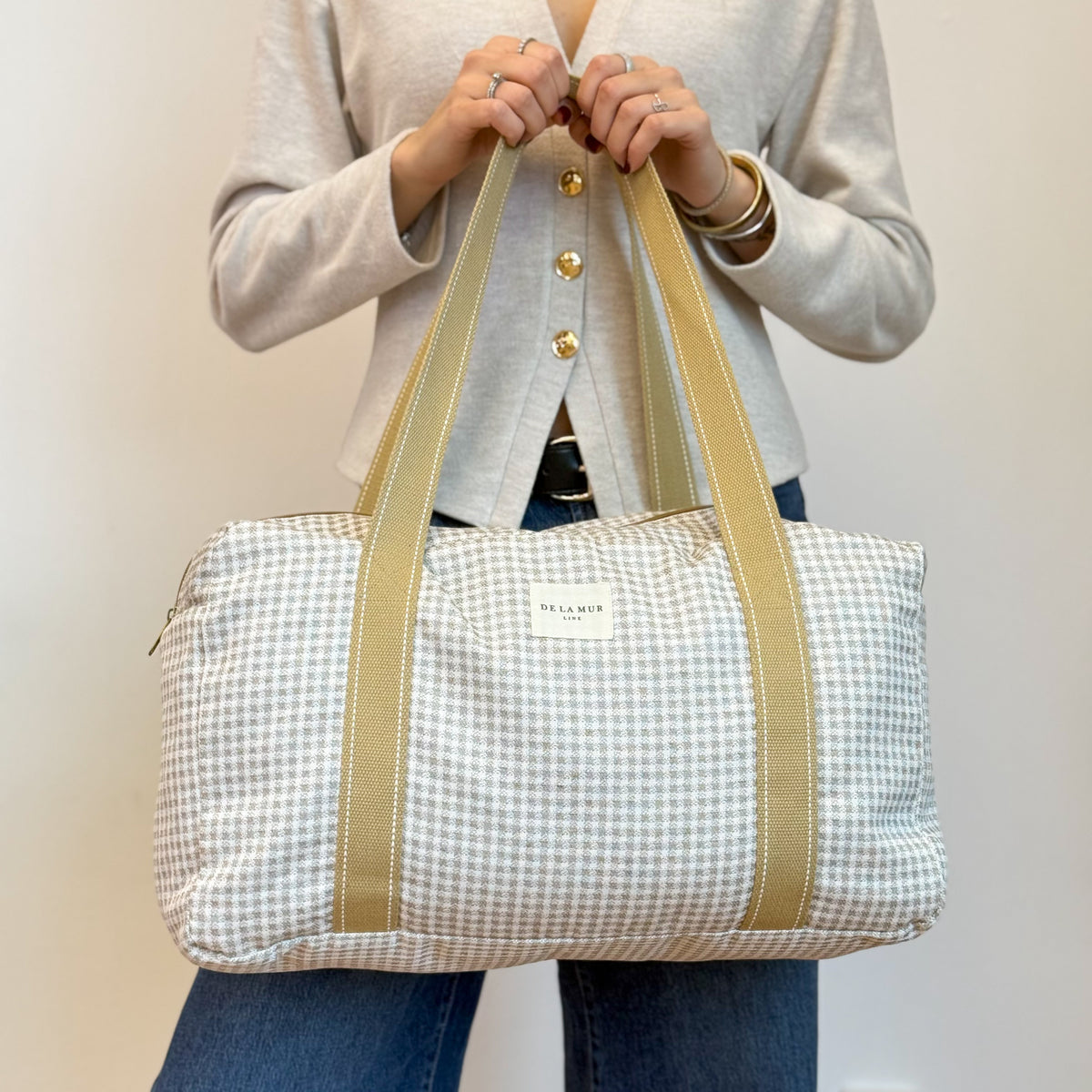 Model holding DE LA MUR gingham jacquard sports bag by the handles
