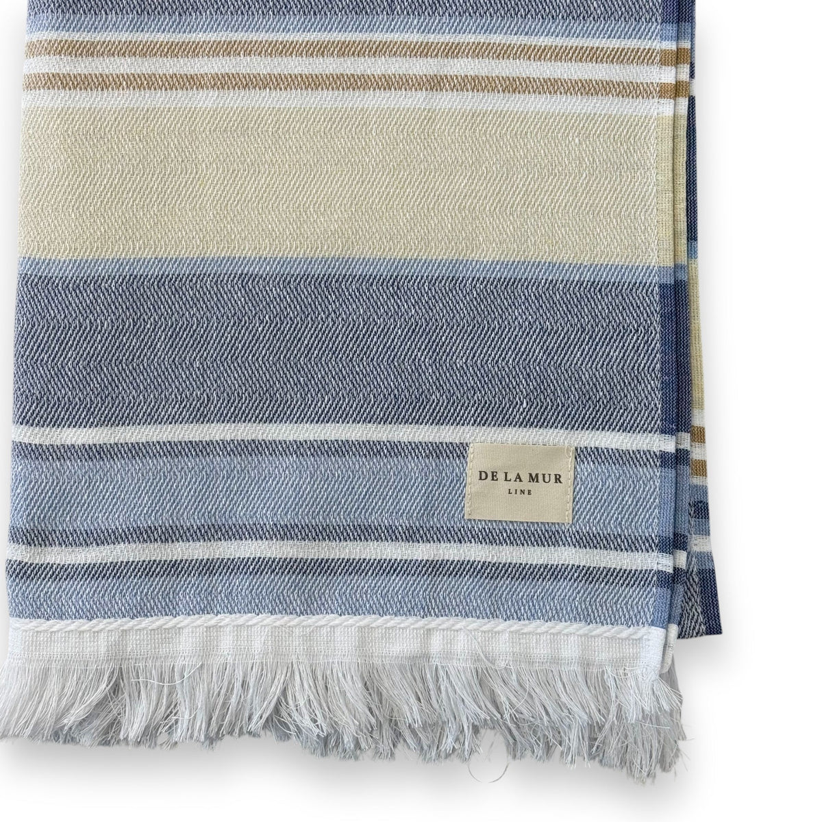 Close-up of DE LA MUR blue and cream striped towel corner, fringe and Line label
