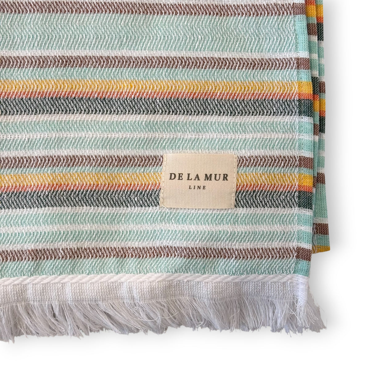 Close-up of DE LA MUR aqua multicolor striped towel corner, fringe and Line label
