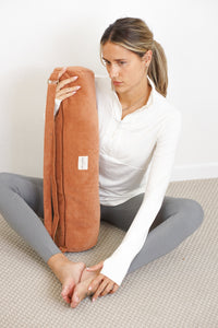 Seated model holding DE LA MUR Barro corduroy yoga mat bag in terracotta, lifestyle shot