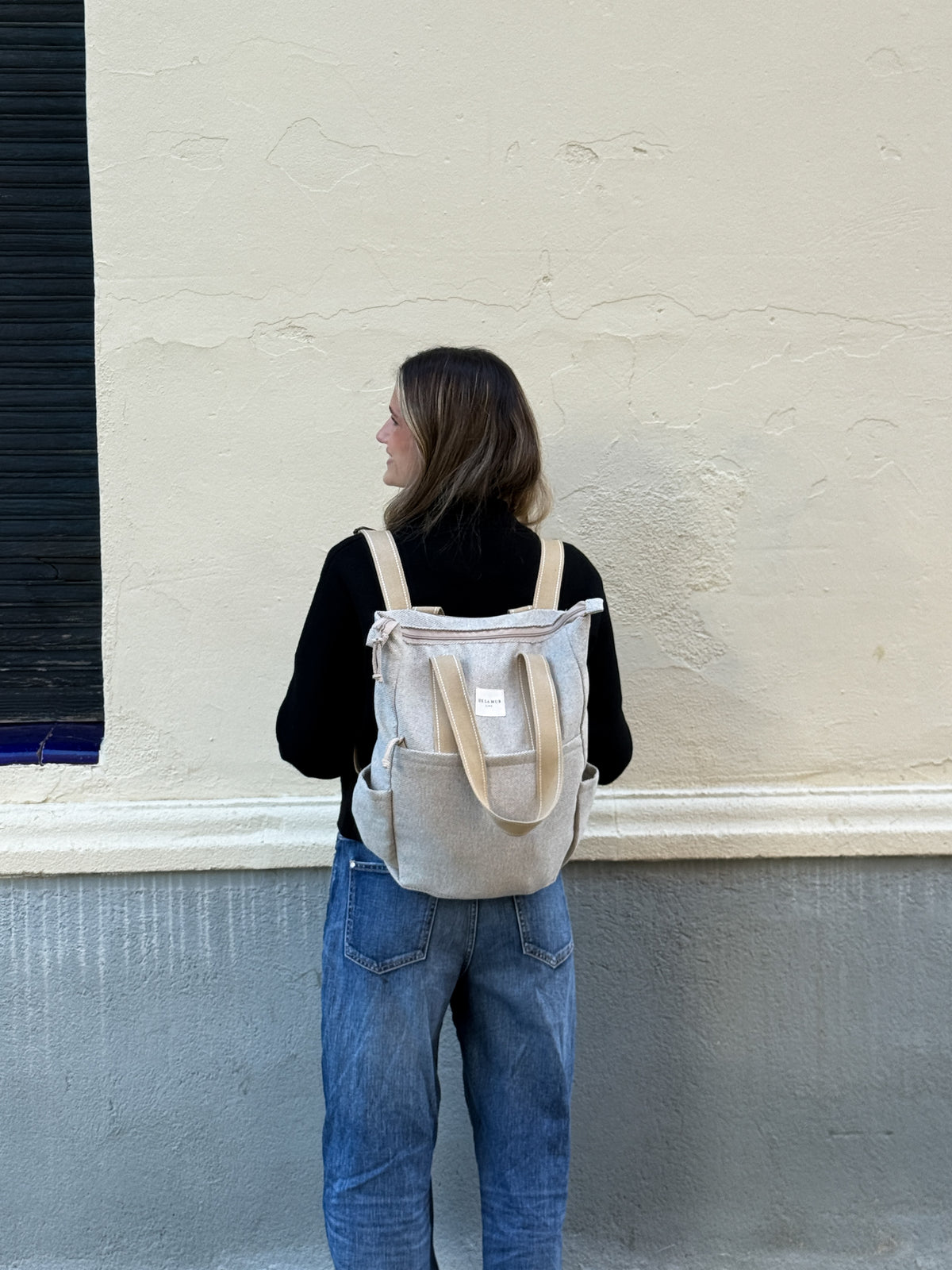 Model wearing the DE LA MUR Sydney beige backpack outdoors, back view