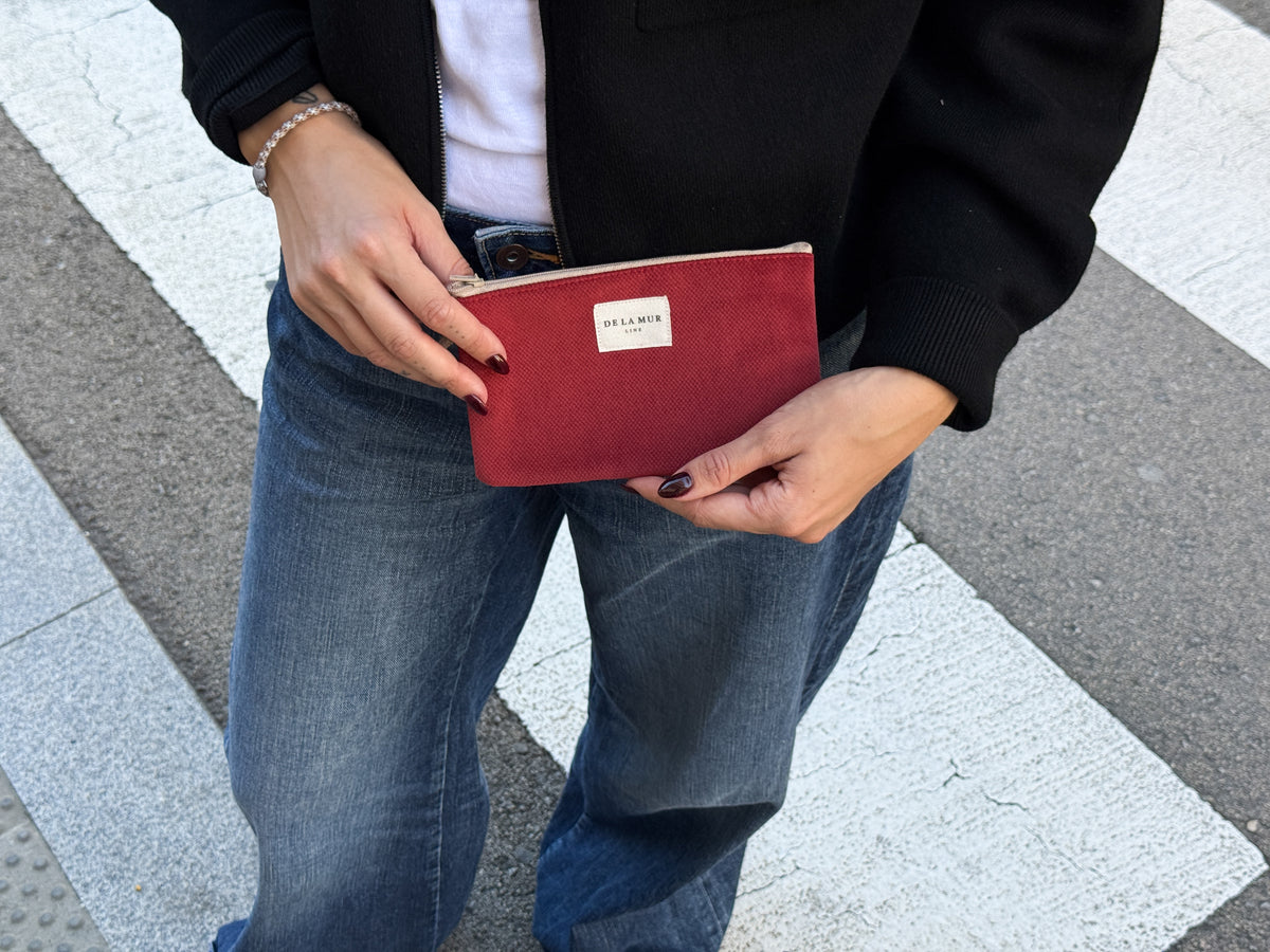 Model holding the DE LA MUR burgundy coin purse outdoors on a crosswalk