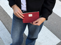 Model holding the DE LA MUR burgundy coin purse outdoors on a crosswalk